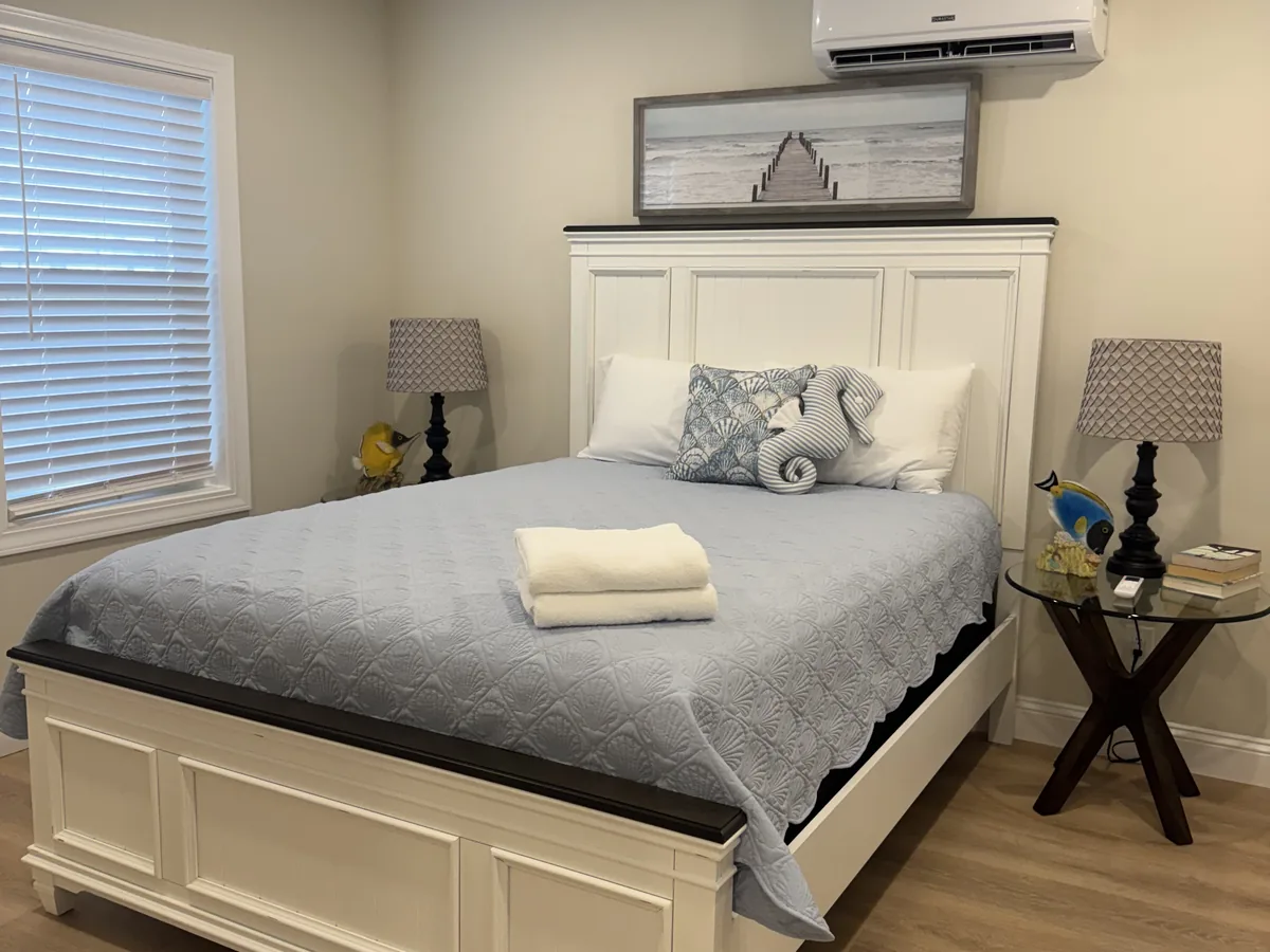 Bedroom with a white headboard, folded towels and dusted nightstands