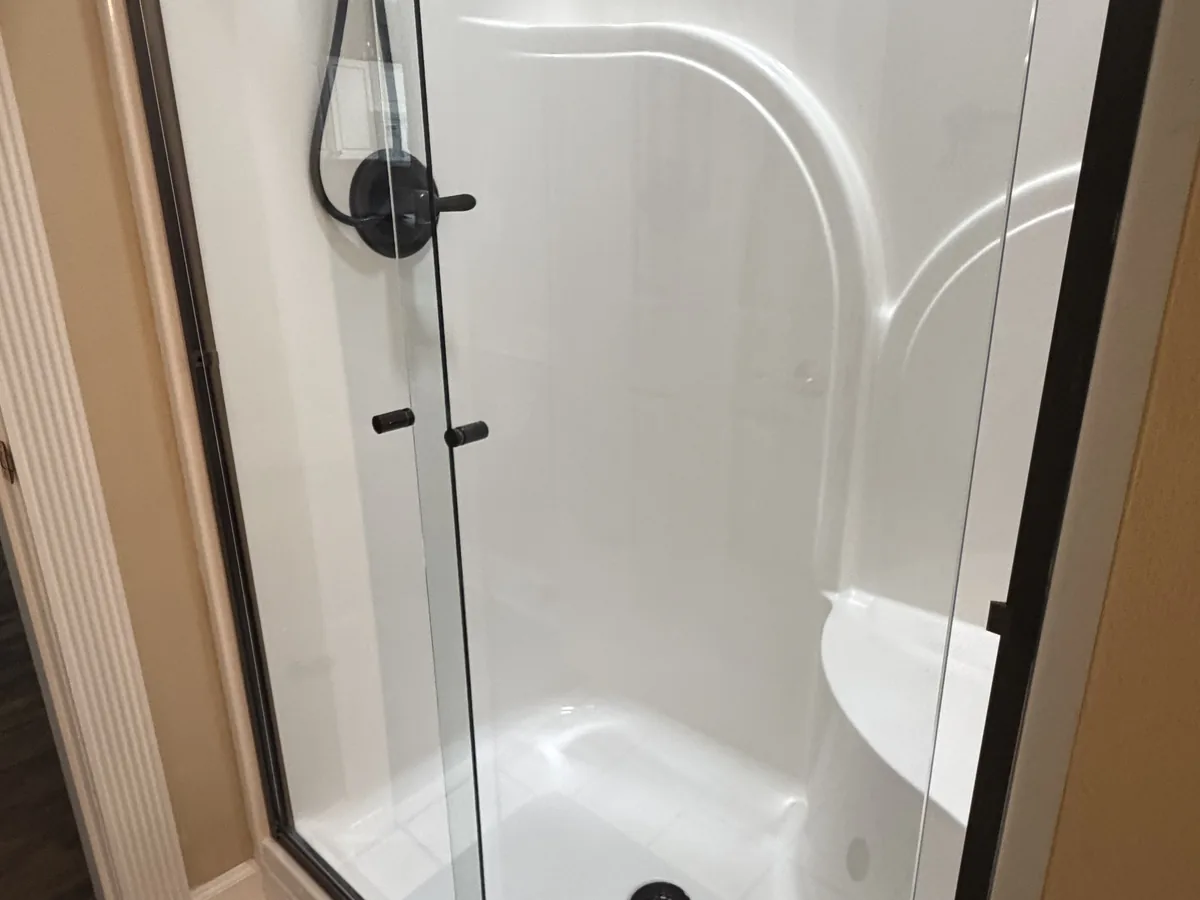 White fiberglass shower stall with a clear glass door and polished fixtures